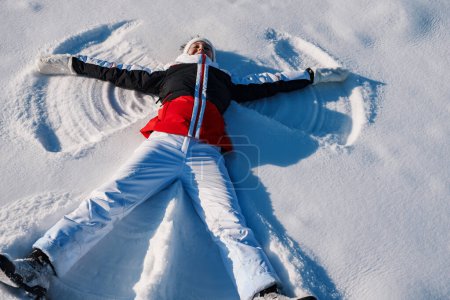 Photo for Happy young woman lying on a snow and doing angel print on snow - Royalty Free Image