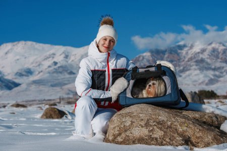 Photo for Young woman tourist with dog in pet carrier on winter mountains background - Royalty Free Image
