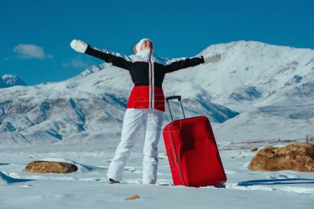 Foto de Feliz joven turista con maleta roja en el fondo de las montañas de invierno - Imagen libre de derechos