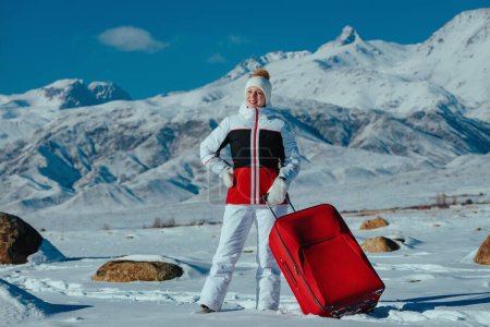 Photo for Young woman tourist with red suitcase on winter mountains background - Royalty Free Image