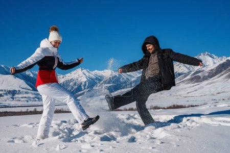 Téléchargez les photos : Jeune homme et femme jouant avec la neige sur fond de montagnes en saison hivernale - en image libre de droit