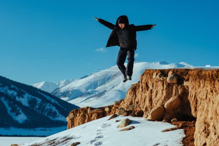 Téléchargez les photos : Un jeune touriste saute de la falaise dans les montagnes - en image libre de droit