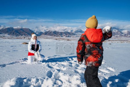 Photo for Young woman and son playing snowballs on mountains background in winter - Royalty Free Image