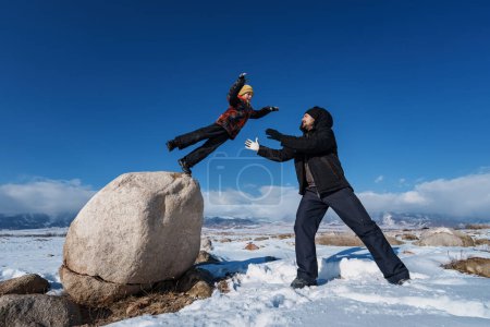 Foto de Niño saltando sobre el padre de piedra grande en las montañas de fondo en la temporada de invierno - Imagen libre de derechos