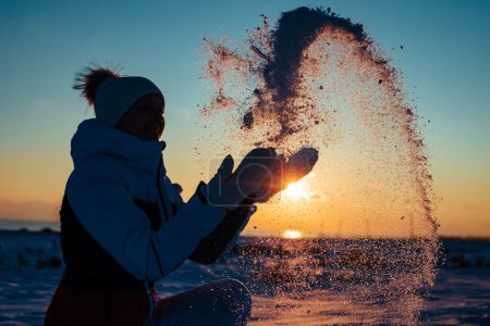 Téléchargez les photos : Jeune femme jetant la neige au coucher du soleil en hiver - en image libre de droit