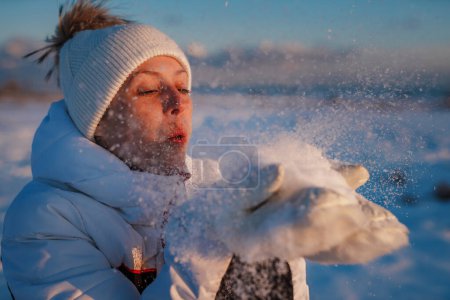 Foto de Mujer joven en chándal sopla copos de nieve de sus mitones - Imagen libre de derechos