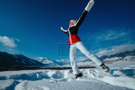 Foto de Joven mujer feliz saltando sobre las montañas de fondo en temporada de invierno - Imagen libre de derechos