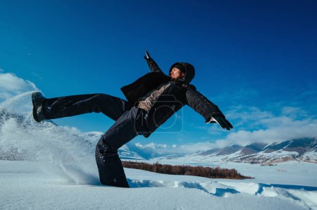 Téléchargez les photos : Jeune homme émotionnel tombant dans la neige sur fond de montagnes en hiver - en image libre de droit