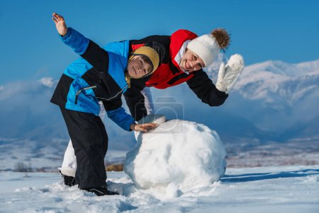 Téléchargez les photos : Joyeux maman et fils faisant bonhomme de neige dans les montagnes - en image libre de droit