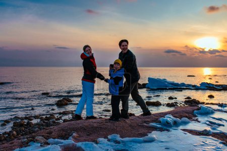 Téléchargez les photos : Famille heureuse avec son fils au bord du lac en hiver au coucher du soleil - en image libre de droit