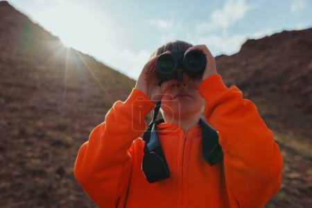 Téléchargez les photos : Portrait de garçon touriste à la recherche de jumelles dans les montagnes - en image libre de droit