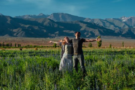 Téléchargez les photos : Joyeux jeune couple profitant du beau temps dans un champ sur fond de montagnes - en image libre de droit