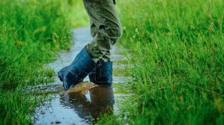 Photo for Boy in rubber boots walking on small stream on summer field - Royalty Free Image