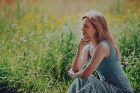 Photo for Thoughtful elegant young woman sitting in a summer meadow - Royalty Free Image