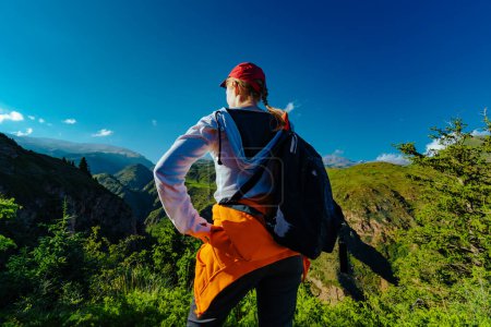 Photo for Young woman hiker with backpack stands on top of mountain and looks at the valley - Royalty Free Image