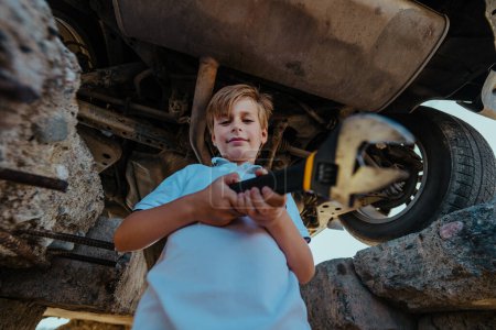 Foto de Lindo niño mecánico automotriz de pie debajo de la parte inferior del coche con llave inglesa - Imagen libre de derechos