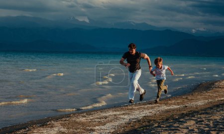 Téléchargez les photos : Père et fils courent sur la plage de sable fin le jour d'été - en image libre de droit