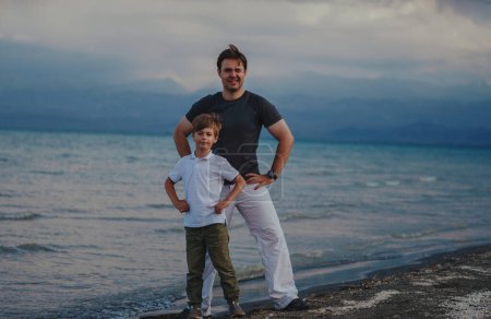 Foto de Feliz padre e hijo de pie en la orilla del lago en el clima ventoso - Imagen libre de derechos