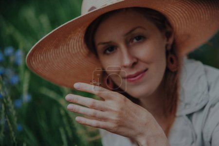Photo for Beautiful young woman in hat with a grasshopper on her arm in summer - Royalty Free Image