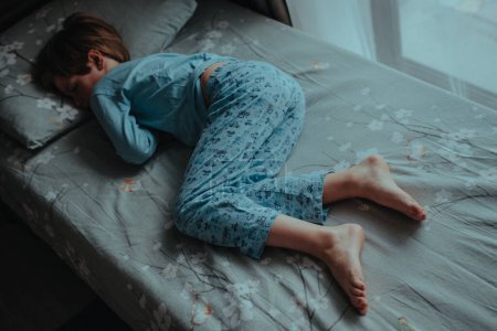 Téléchargez les photos : Garçon en pyjama dormant au lit sans couverture - en image libre de droit