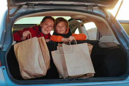 Téléchargez les photos : Bonne mère et enfant tenir sacs à provisions en papier dans la voiture à la lumière du coucher du soleil - en image libre de droit