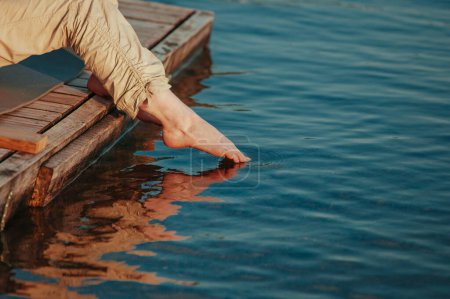 Foto de El pie de mujer toca la superficie del agua al atardecer - Imagen libre de derechos
