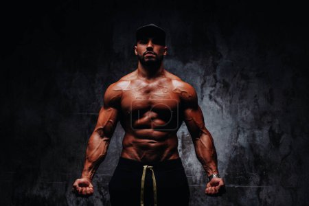 Photo for Young strong man bodybuilder in cap on stone wall background - Royalty Free Image