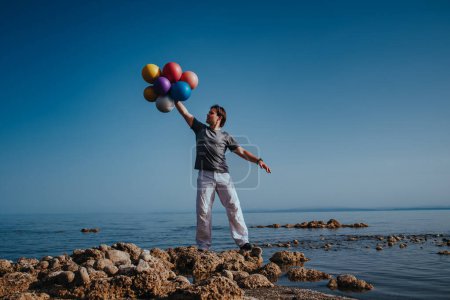 Foto de Young happy man with balloons on the shore of lake - Imagen libre de derechos