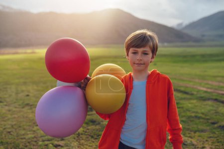 Foto de Happy boy with balloons in the mountains at sunset - Imagen libre de derechos