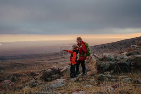 Foto de Turista mujer con hijo de pie en la montaña y mirando hacia la distancia - Imagen libre de derechos