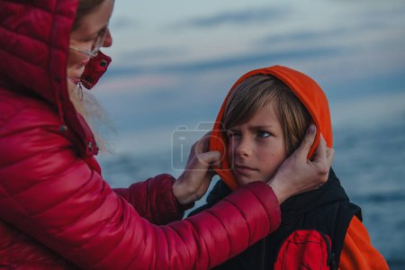 Mother dressing naughty child in cold windy weather on lake shore
