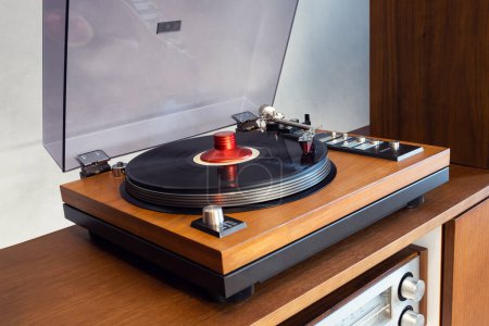 Téléchargez les photos : Vintage stéréo tourne-disque vinyle avec couvercle en plastique ouvert et socle en bois debout au-dessus de l'amplificateur. Accueil Équipement audio rétro. - en image libre de droit