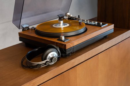 Téléchargez les photos : Lecteur de disque vinyle stéréo vintage avec couvercle en plastique ouvert et écouteurs debout sur une étagère en bois. Accueil Système audio rétro avec haut-parleurs. - en image libre de droit