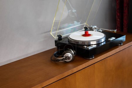 Foto de Reproductor de discos de mesa giratoria estéreo vintage con disco de colores, auriculares y abrazadera de peso de pie en el estante de madera - Imagen libre de derechos