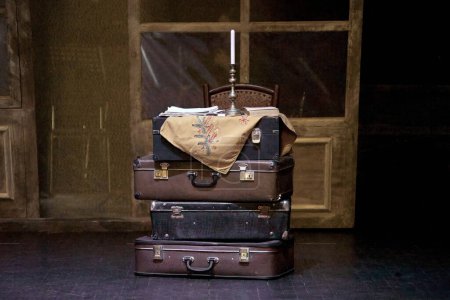Image of a bunch of suitcases on a theater stage with candles in a candlestick