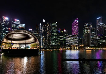 Foto de Sudeste Asiático, Singapur, noviembre de 2022: Rascacielos de negocios de la ciudad de Singapur y distrito financiero con iluminación nocturna. Coloridas luces de la ciudad reflejadas en el agua de la bahía. Hermoso paisaje urbano. - Imagen libre de derechos