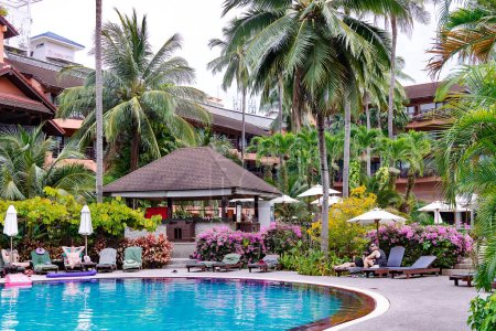 Téléchargez les photos : THAILAND, PHUKET, FEBRUARY, 2023: Swimming pool among a beautiful garden with tall palm trees on the territory of Patong Merlin Hotel in Phuket, Thailand - en image libre de droit
