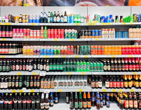 Photo for LATVIA, RIGA, APRIL, 2023: Glass and aluminum bottles of popular types of beer on shelves for sale in big food section. Shelves with alcoholic beverages. - Royalty Free Image