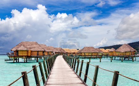 Téléchargez les photos : Bungalows au-dessus de l'eau s'étendant et un pont en bois sur la lagune de l'île de Bora Bora, Tahiti. Destination lune de miel romantique. - en image libre de droit