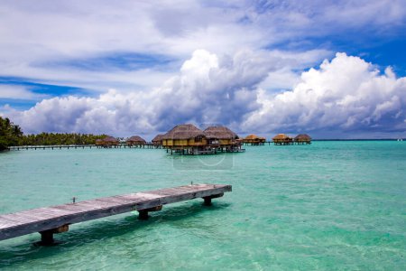 Téléchargez les photos : Bungalows au-dessus de l'eau s'étendant et un pont en bois sur la lagune de l'île de Bora Bora, Tahiti. Destination lune de miel romantique. - en image libre de droit