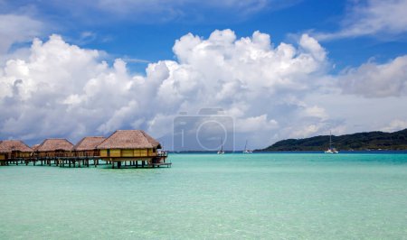 Téléchargez les photos : Bungalows sur pilotis s'étendant à travers la lagune et quelques catamarans dans une baie tranquille de l'île de Bora Bora, Tahiti. Destination lune de miel romantique. - en image libre de droit