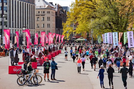 Foto de LATVIA, RIGA, 23, ABRIL, 2023: Bailarines con disfraces nacionales letones están en plataformas especiales y se reúnen con personas que corren en la Maratón de Rimi Riga 2023. La maratón es un evento anual. - Imagen libre de derechos
