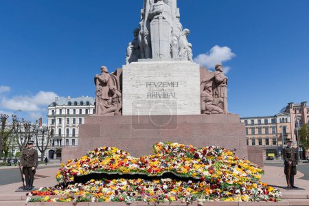 Téléchargez les photos : LETTONIE, RIGA, 15, MAI 2023 : La garde d'honneur près d'une variété de fleurs printanières se trouve sur le monument de la liberté sur le boulevard de la liberté dans la vieille ville de Riga, capitale de la Lettonie. UE. - en image libre de droit