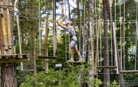 Foto de LATVIA, JURMALA, 24, JUNIO, 2023: Dzintari Adventure Climbing Forest Park con varios columpios para niños y marco de escalada en Jurmala. Letonia. Concepto infantil saludable y deportivo. - Imagen libre de derechos