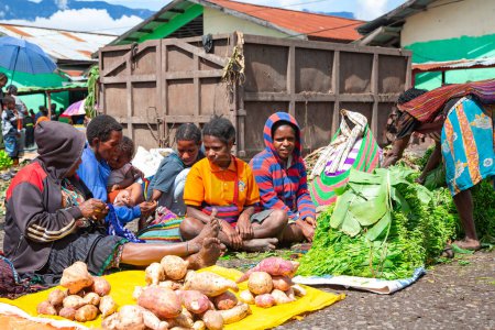 Foto de INDONESIA, PAPUA NUEVA GUINEA, WAMENA, IRIAN JAYA, 20 AGOSTO 2019: Papuans woman sell sweet potatoes and other vegetables on the street market in Wamena, New Guinea, Indonesia
. - Imagen libre de derechos