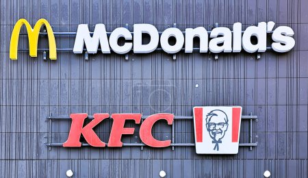 Foto de LATVIA, RIGA, 15, ENERO, 2024: McDonald 's y el logotipo de KFC en una fachada rayada del edificio del centro comercial Akropole en Riga, Letonia. La Corporación McDonald 's es la cadena más grande del mundo de restaurantes de comida rápida para hamburguesas. - Imagen libre de derechos