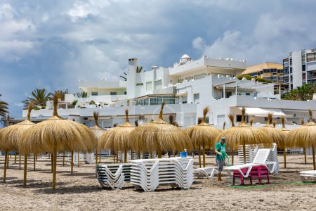 Photo for SPAIN, MARBELLA, 25, MAY, 2023: A beach worker washes sand from beach chairs with a jet of water in Marbella, Spain. - Royalty Free Image