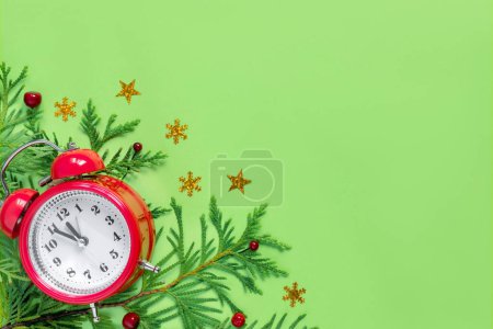 Photo for Alarm clock  with tree branches on green paper background. 5 minutes before the New Year. Creative greeting car - Royalty Free Image