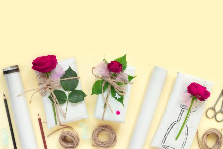 Téléchargez les photos : Gifts in paper wrapping, set of vintage yellow package paper, rolls, ropes and pencils for decoration. Bouquet of red roses on yellow vintage background. - en image libre de droit
