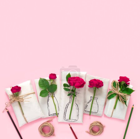 Téléchargez les photos : Set of wrapping paper and flowers for handmade on pink background. Homemade craft box gifts with painted vase, bouquet of red roses - en image libre de droit